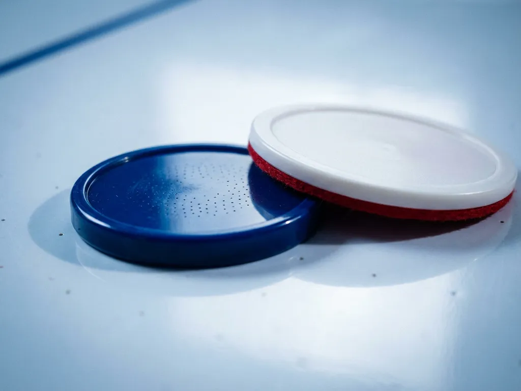 Luchthockeypuck en slagmallet op wit tafelvlak met zichtbare luchtgaatjes, close-up met blauwe en witte tinten.