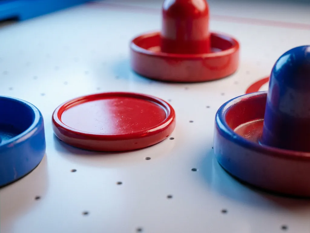 Rode luchthockeypuck en twee strikers op wit tafelvlak met zichtbare luchtgaatjes, macro close-up.