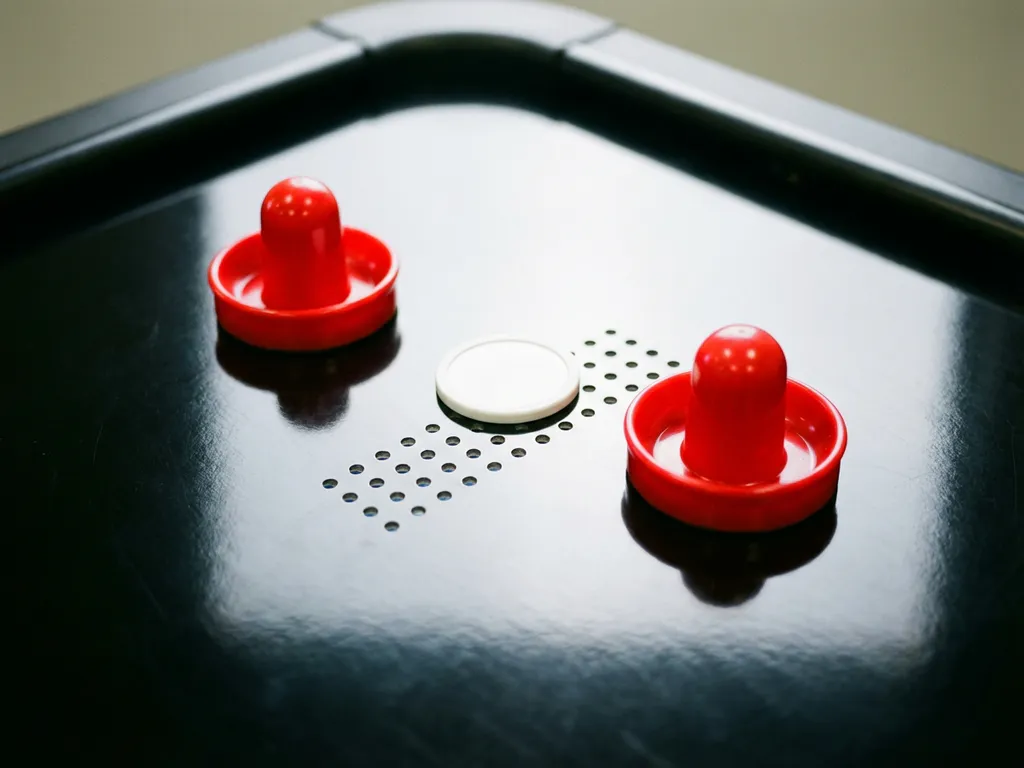 Twee rode air hockey-strikers en een wit puck op een glanzend zwart air hockey-tafeloppervlak, bovenaanzicht.