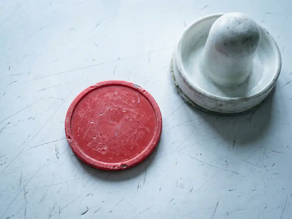 Versleten luchthockeypuck en rode slagmallet op bekraste witte luchthockeytafel, bovenaanzicht met scherpe materiaaltexturen.