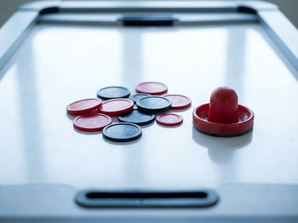 Meerdere luchthockeypucks in verschillende maten op een glanzend wit luchthockeytafel, met een rode slaghamer ernaast.